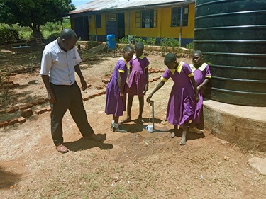 Kubar schoolgirls drinking form the school's new rainwater tank.