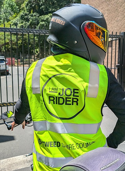 Motorcyclist wearing a high visibility vest with the 'I Am Joe Rider' and Tweed Shire Council logos printed on the back.