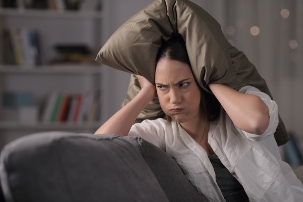 Unhappy lady covers ears with pillow to keep out noise.